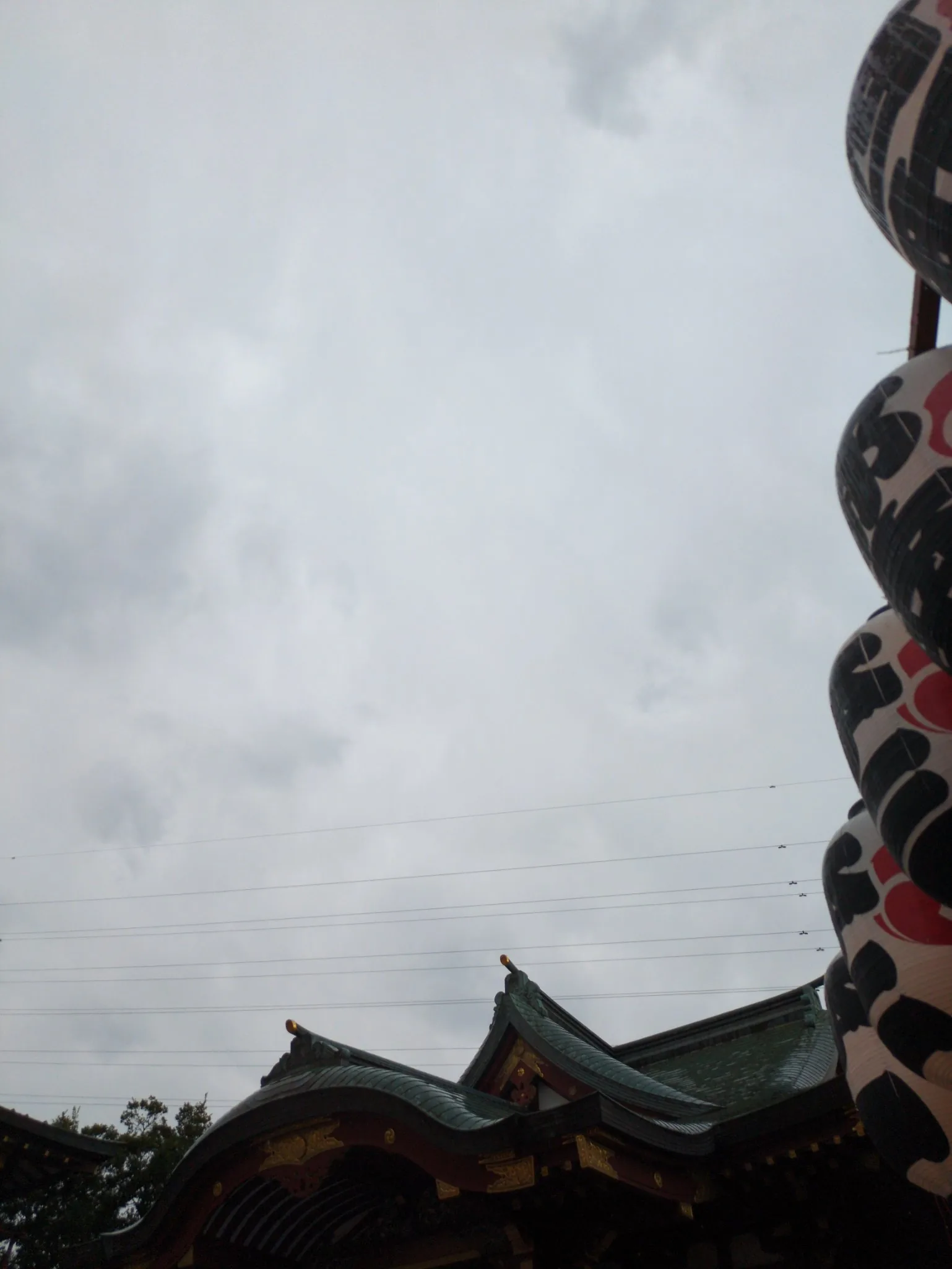 雨雲の下の羽田神社。社殿の屋根と祭り提灯