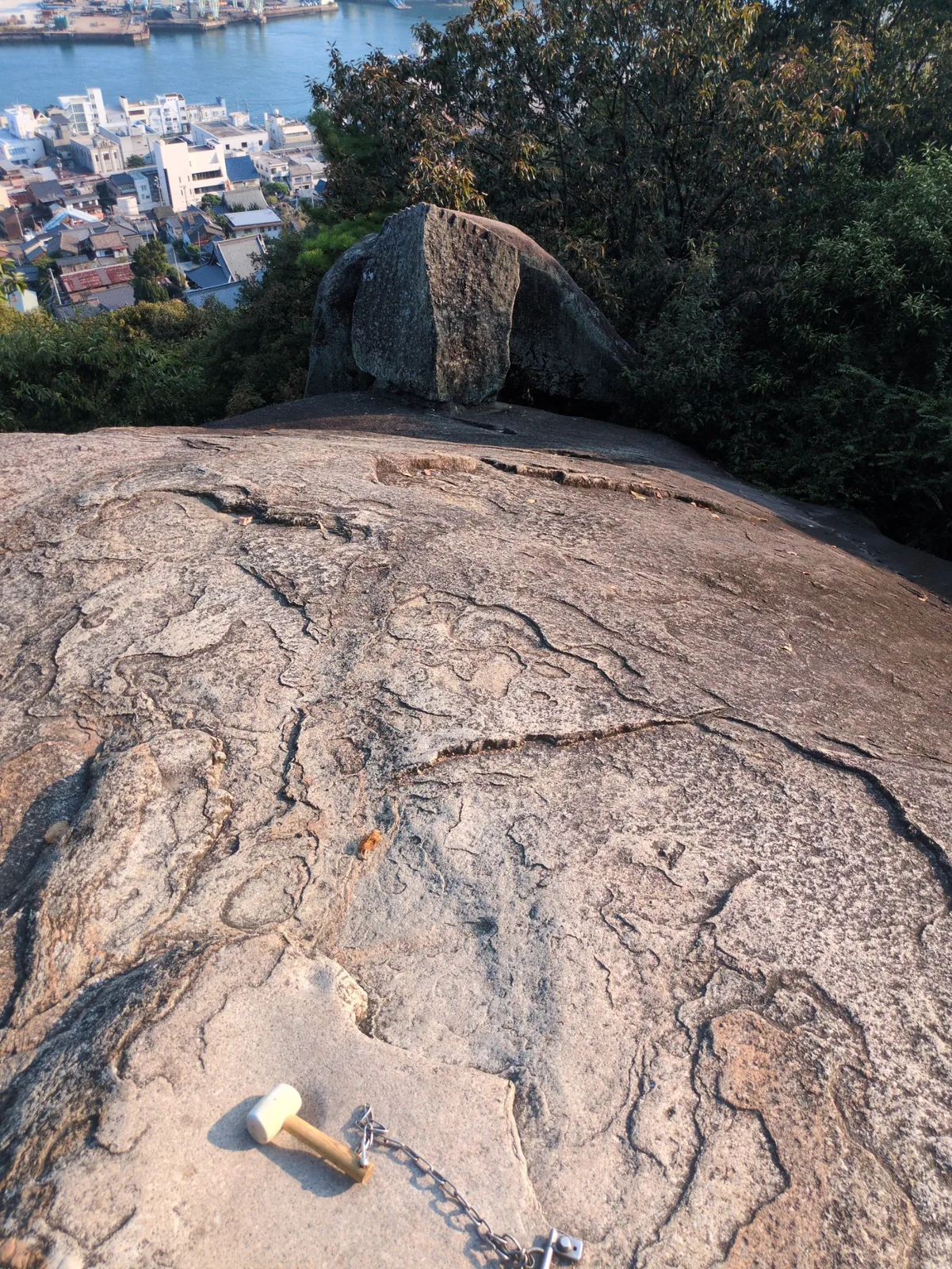 千光寺山の鼓岩。手前に鎖でつないだ木槌が置かれ、奥の岩に矢穴が一直線に並ぶ。眼下は尾道の町と海峡